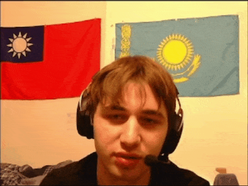 a man wearing headphones and a microphone stands in front of flags