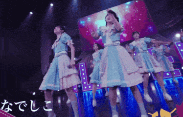 a group of girls in blue and white dresses are dancing on a stage in front of a large screen