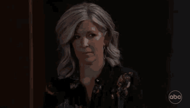 a woman with gray hair and a floral shirt is standing in a dark room .