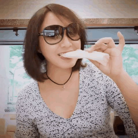 a woman wearing sunglasses and a necklace is eating a piece of food .