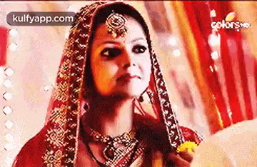 a bride in a red and gold dress is holding a veil and looking at the camera .