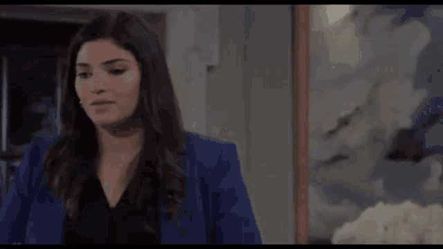 a woman in a blue jacket is standing in front of a painting in a living room .