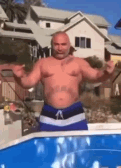 a shirtless man in blue swim trunks is standing next to a swimming pool .