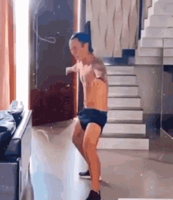 a man without a shirt is dancing in a living room in front of stairs .