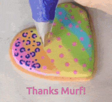 a heart shaped cookie is being decorated with frosting and the words thanks muff are below it