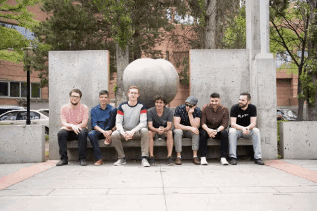 a group of men are sitting on a bench with one wearing a black shirt that says ' a.p.m. '