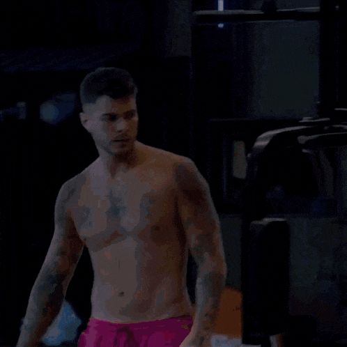 a shirtless man wearing pink shorts is standing in a gym .