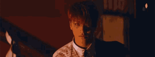 a man with red hair is standing in a dark room with a shadow on his face .