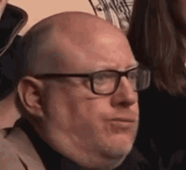 a bald man with glasses and a beard is making a face .