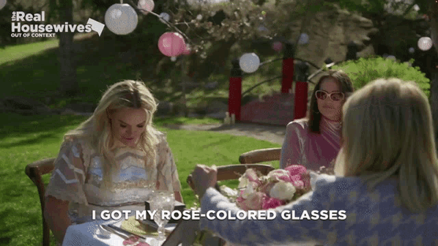 three women are sitting at a table with the words " i got my rose-colored glasses " on the screen