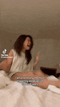a woman is sitting on a bed and crying while making a tiktok video .