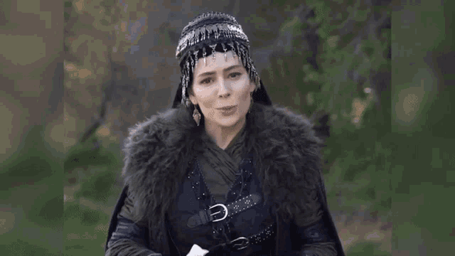 a woman in a fur coat is standing in a forest .
