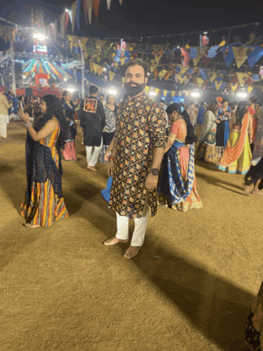 a man with a beard stands in a crowd of people at a festival wearing a shirt that says ' pk '