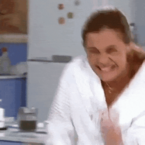 a woman wearing a white robe is smiling in a kitchen
