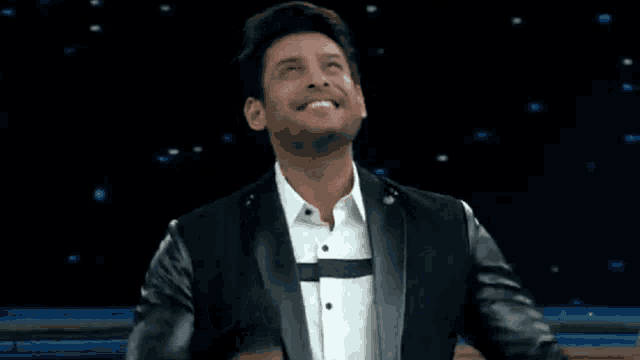 a man in a black jacket and white shirt is smiling and dancing