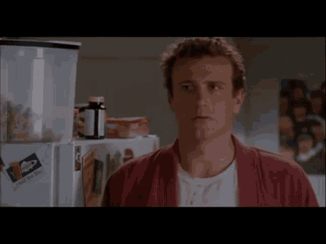 a man in a red robe is standing in front of a fridge with a bottle of pills on it .