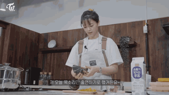a woman in an apron is preparing food in a kitchen with a carton of milk in the foreground