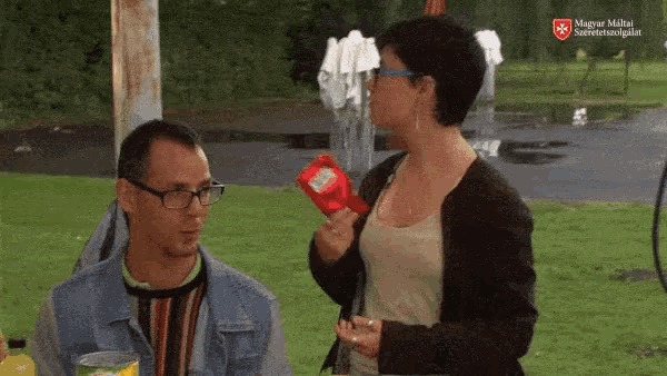 a man and a woman are talking in a park and the woman is holding a bag of ritz crackers
