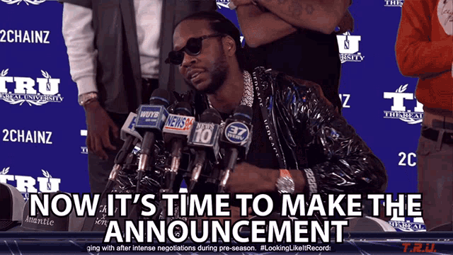 a man stands in front of a bunch of microphones with the words now it 's time to make the announcement below him