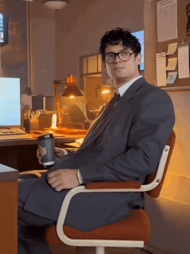 a man in a suit and tie sits in an office chair holding a cup of coffee