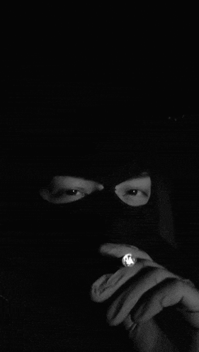 a man wearing a ski mask is smoking a cigarette in a black and white photo .