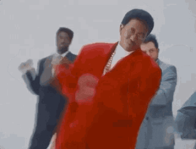 a man in a red suit and tie is dancing in front of a group of men in suits and ties .
