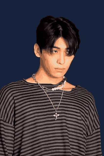 a young man wearing a striped shirt and a necklace is looking at the camera .