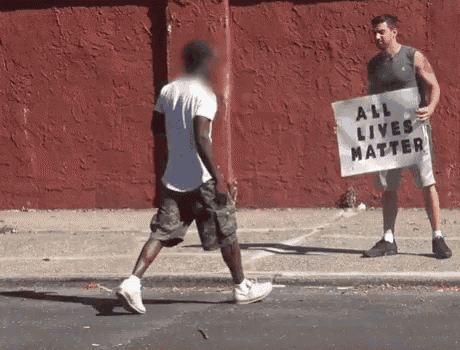 a man holding a sign that says all lives matter talks to another man