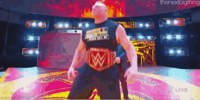 a man wearing a wrestling belt with the letter w on it is standing on a stage .