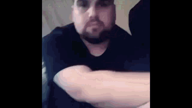 a man with a beard is sitting on a couch with his arms crossed and looking at the camera .