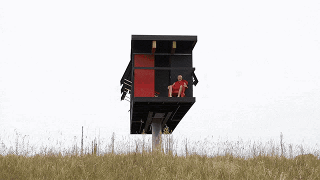 a man sits on a balcony of a building with a red door