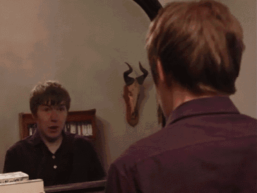 a man is looking at his reflection in a mirror with horns on the wall behind him