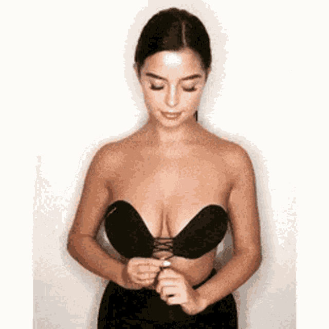 a woman is wearing a black bra with a lace up front and is adjusting it .