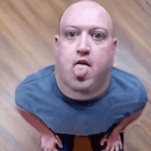 a bald man wearing a blue shirt is making a funny face .