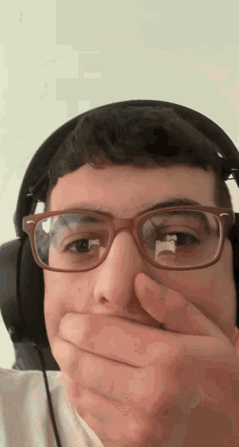 a young man wearing glasses and headphones is covering his mouth with his hand