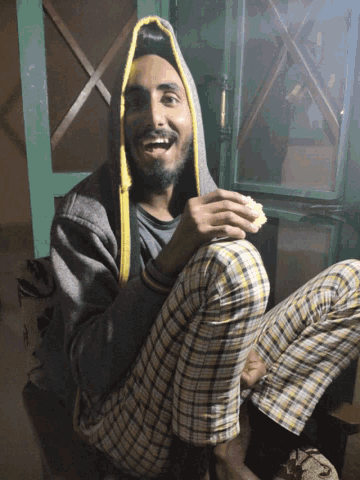 a man wearing plaid pants and a hooded jacket is smiling and holding a piece of food