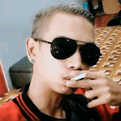 a man wearing sunglasses is smoking a cigarette in a room .