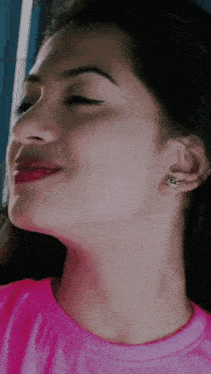 a close up of a woman 's face with a pink shirt and earrings