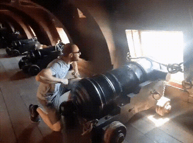a man is kneeling down in front of a cannon with a window in the background