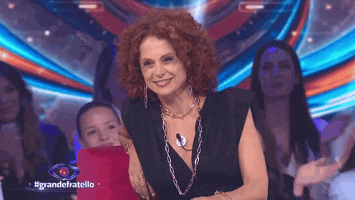 a woman with red curly hair is smiling in front of a sign that says #grandefratello
