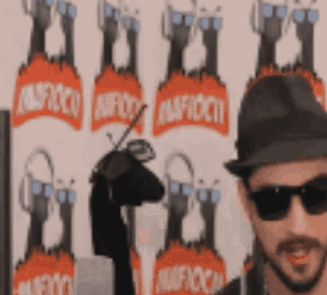 a man wearing sunglasses and a hat stands in front of a wall that says ' aafoch '