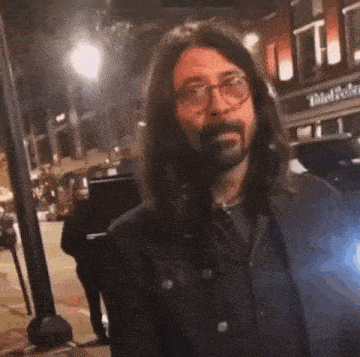 a man with long hair and a beard is standing on a street .