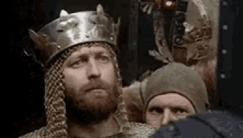 a man with a beard wearing a crown and a helmet is standing in a dark room .
