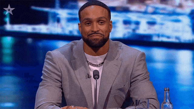 a man in a suit is sitting at a table with a microphone