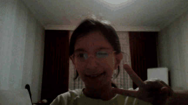 a young girl wearing glasses and a green shirt is giving a peace sign