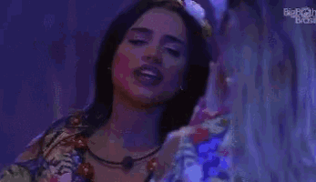 a woman is singing into a microphone while wearing a necklace and a floral shirt .