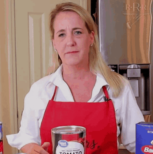a woman wearing a red apron holds a can of tomato sauce