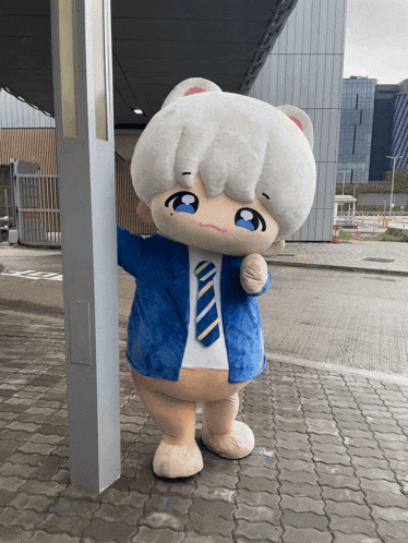 a mascot in a blue jacket and tie is standing on a brick sidewalk