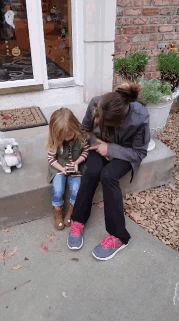 a woman and a little girl are sitting on a porch looking at a phone