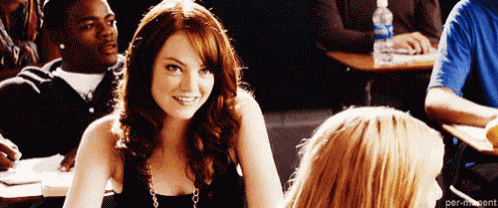 a woman is smiling in a classroom while sitting at a desk next to another woman .